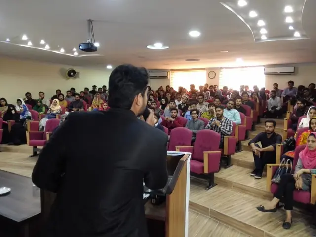 Usman Saeed speaking from the podium to a full auditorium at Punjab University, Lahore